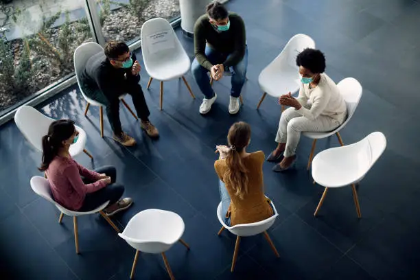 Photo of Above view of people wearing face masks during group therapy due to coronavirus pandemic.