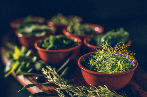 Low key of different green herbs on a rustic wooden board with focus on the fennel, selective focus and grain added. Part of a rustic fresh herb - series and E+ and S+ collection