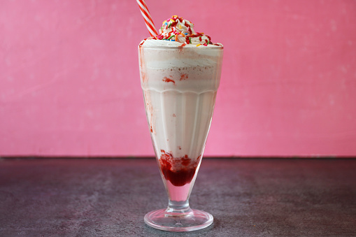 Stock photo showing a strawberry smoothie / milkshake drink, served in an American diner-style knickerbocker glass. This drink has been made with pureed strawberries, milk and whipped cream and topped with hundreds and thousands.