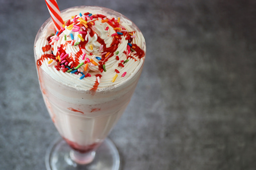 Stock photo showing a strawberry smoothie / milkshake drink, served in an American diner-style knickerbocker glass. This drink has been made with pureed strawberries, milk and whipped cream and topped with hundreds and thousands.