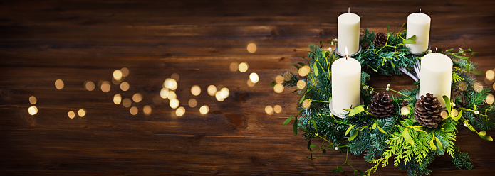 Advent wreath on dark wooden table with golden bokeh lights and christmas mood. Horizontal background with space for text.