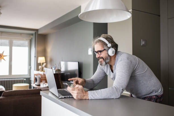 istock Senior man using a laptop and mobile phone at home in pajamas 1286339813