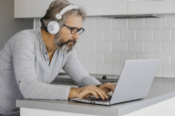 istock Senior man using a laptop at home in pajamas 1286340033