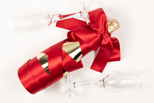 gift bottle of champagne in gold foil wrapped in a red silk ribbon and two glasses on a white background
