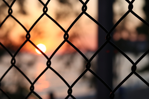 View of a sunset through a silhouette fence in urban environment