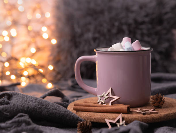 fairy lights background, hot cocoa with marshmallows, pink coffee cup, cinnamon sticks, cones, wooden stars, soft plaid blanket for cozy atmosphere at home during christmas and new year holidays. soft selective focus bokeh - kakao heißes getränk fotos stock-fotos und bilder