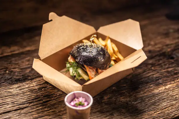 Photo of Tasty black burger takeaway in a box of recycled paper on wooden board