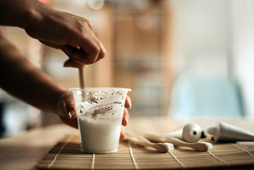 side view of young women hands holding a cup of handmade toothpaste and stirring on it