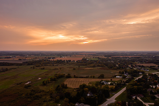 A beautiful aerial sunset sky and landscape photograph of a pink and orange colored clouds over rural farm land and homes near Slinger, Wisconsin.