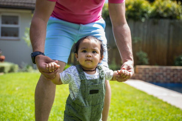 istock Father holding his daughters hands as she walks on the grass 1286356018