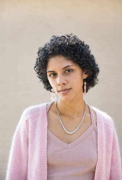 Portrait of a Young Hispanic Puerto Rican Woman in Orlando This is a portrait of a young Hispanic Puerto Rican woman in her 20s standing outdoors in Orlando, Florida. She has short curly hair and wears a pink sweater. puerto rican ethnicity stock pictures, royalty-free photos & images