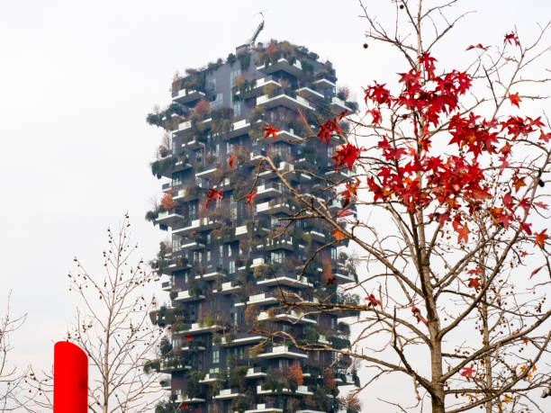 Milan, Lombardy, Italy.  December 2019.    Trees with autumn leaves in front of a residential building with terraces where plants are planted for oxygen generation.
