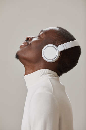 Side view of African man in wireless headphones enjoying the music isolated on grey background