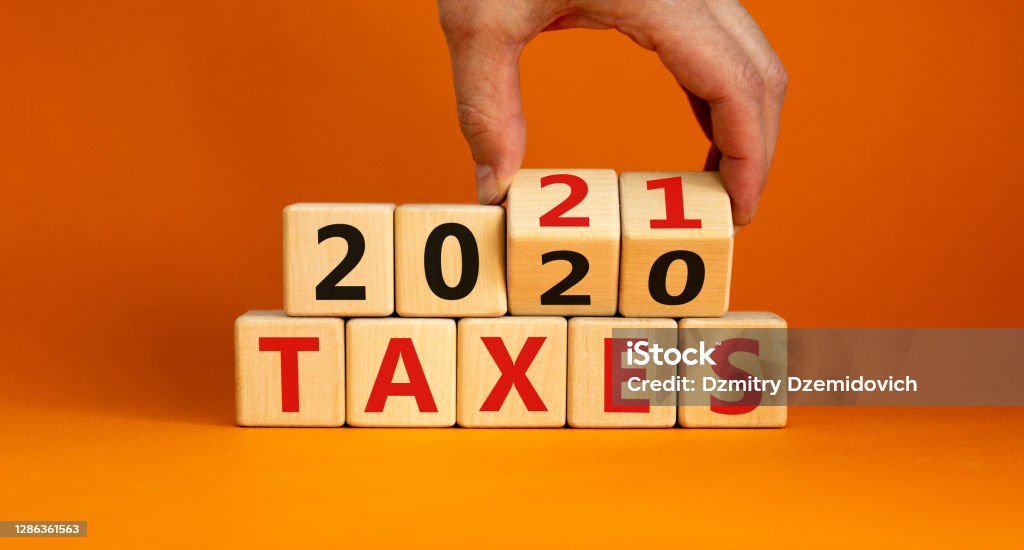 Business concept of planning 2021. Male hand flips wooden cubes and changes the inscription 'Taxes 2020' to 'Taxes 2021'. Beautiful orange background, copy space. Tax Stock Photo