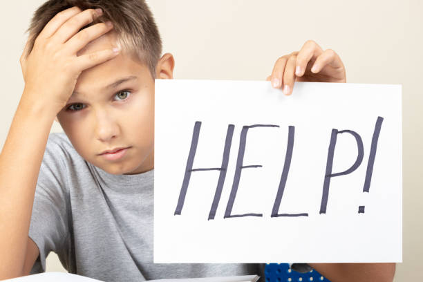 istock Learning difficulties, school, quarantine education concept. Tired frustrated boy sitting at table and holding card with word Help 1286366640