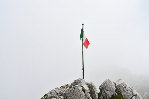 Tricolour flag fluttering over the apex of mountains partially covered by low clouds