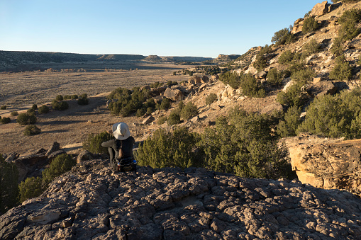 Sitting on a large boulder, a woman enjoys the morning with long shadows along the cliffs of the Picket Wire Canyonlands in the Purgatoire River valley in the Comanche National Grasslands of southeast Colorado.