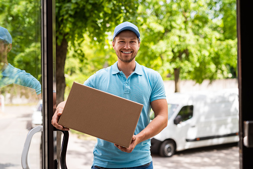 Fast delivery to your home. Smiling courier holding a package in the cardboard box