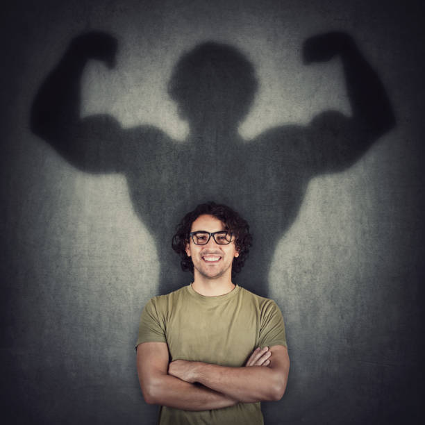 istock Confident young man shadows transforms into a muscular person on the wall as metaphor for inner strength. Motivated guy imagine flexing big biceps as super power. People self defense concept. 1286380919
