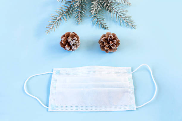 istock Protective medical mask, spruce branches and pine cone on blue background. Christmas and New Year during pandemic of coronavirus infection. Flat lay, top view, copy space. 1286383845