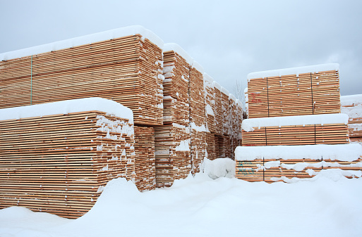 A lumber mill with piles of produced boards and construction material. Image taken in winter after fresh snow.