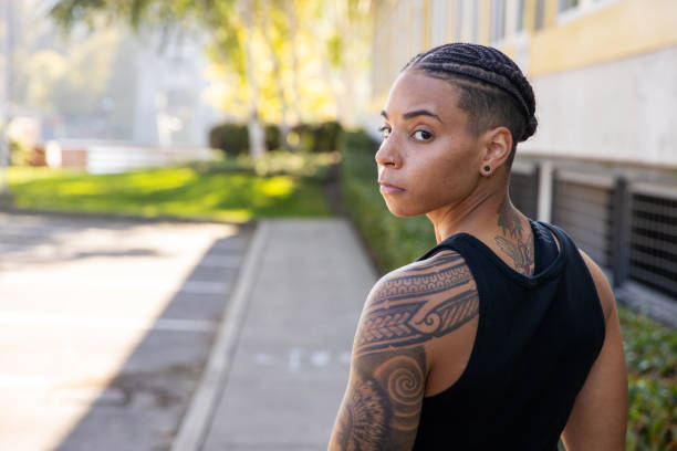 Strong, tattooed African American woman looking back over her tattooed shoulder Fit African American woman with braided black hair looking over her tattoo covered shoulder back shoulder tattoos for women pictures stock pictures, royalty-free photos & images