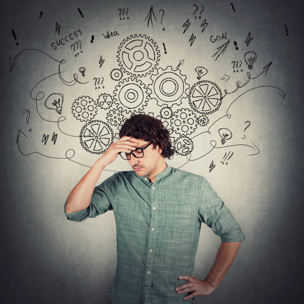 istock Confused and pensive businessman, keeps hand to forehead, thinking for solutions to solve difficult tasks. Pondering man puzzled focuses his mind. Gear cogwheels and arrows as thoughts around head. 1286384962
