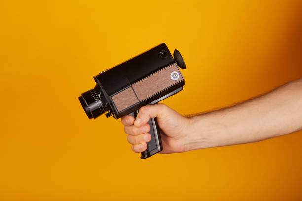 operator trzymający staroświecki analogowy super8, 8mm film kamery filmowej na żółtym tle. celowanie w kamerę jak pistolet - 8mm camera zdjęcia i obrazy z banku zdjęć