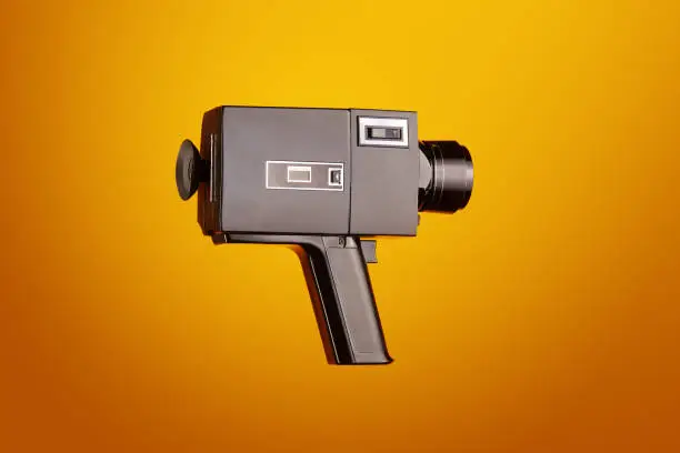 Photo of Old fashioned analog Super8, 8mm film movie camera against yellow background