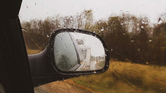 Car with trailer travel trip active vacation in rainy day, indoor view from car to front side window to outdoor back view mirror caravan trailer reflection. Journey and caravan travel concept