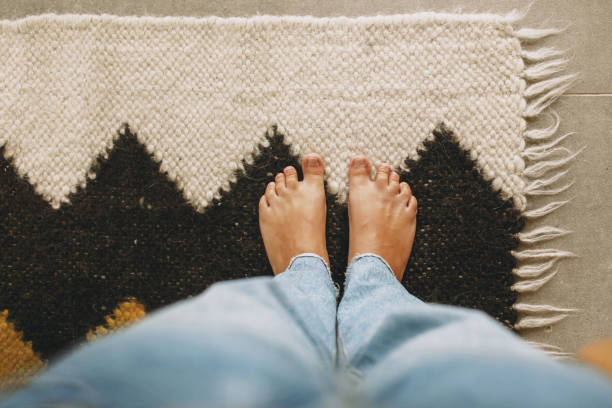 Feet on cozy woolen rug on background of concrete floor. Woman barefoot standing on modern rug Feet on cozy woolen rug on background of concrete floor. Woman barefoot standing on modern rug in comfortable stylish home, top view. Cozy warm moments heat home interior comfortable human foot stock pictures, royalty-free photos & images