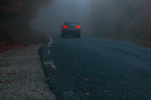 Lonely car on the mountain road covered in thick fog with red lights  on