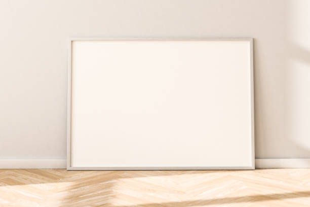 istock Horizontal empty Picture Frame on parquet floor leaning against bright wall. Sunlight flooding in from the left. 1286395561
