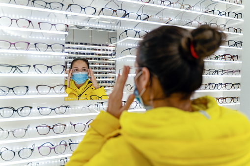 Customer wearing face mask trying on reading glasses in an optical store