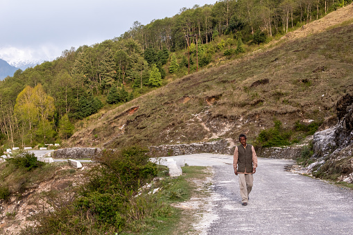 Munsyari, Uttarakhand, India - April 2019: An Indian man wearing a grey waistcoat walking down a mountain road in a Himalayan village.