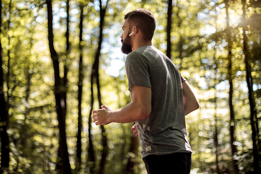 Young man with bluetooth headphones jogging in forest
