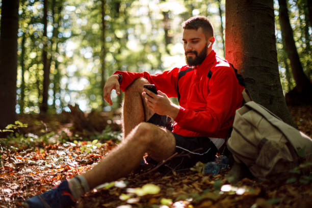 retrato de jovem sorridente com fones de ouvido bluetooth usando celular na floresta - telephone nature mobile phone autumn - fotografias e filmes do acervo