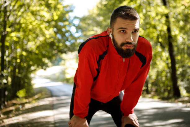 istock Portrait of young handsome man with bluetooth headphones resting while jogging in forest 1286401556