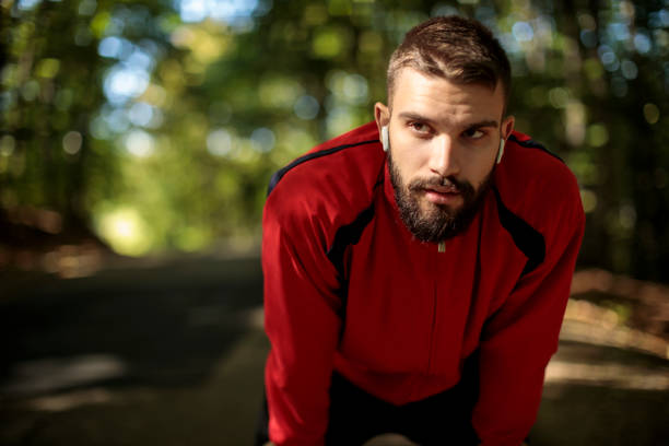 istock Portrait of young handsome man with bluetooth headphones resting while jogging in forest 1286401664