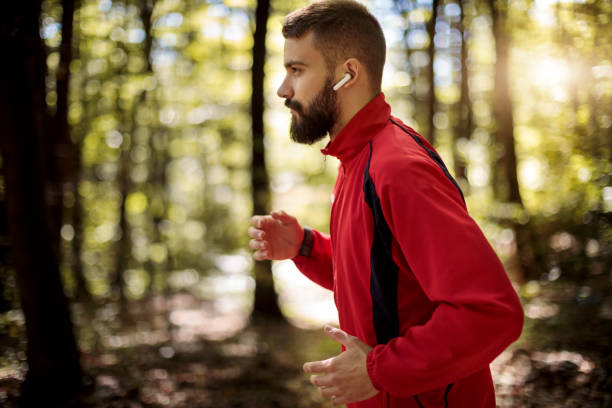 istock Young man with bluetooth headphones jogging in forest 1286402841