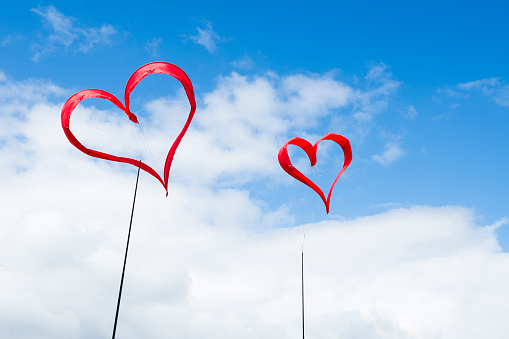 Two red heart shaped kites on a blue sky with white clouds