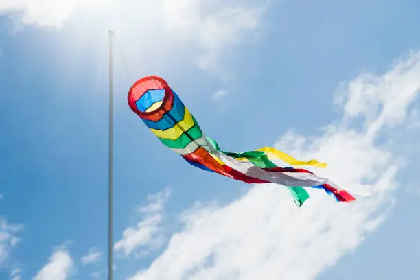 Colorful sindsock blowing and showing the direction of the wind on a blue and sunny sky