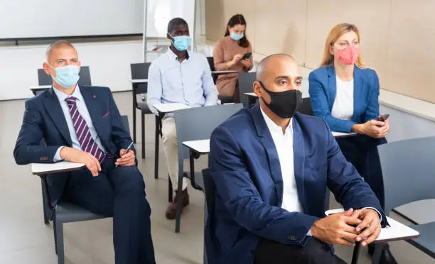 International group of business people in protective masks listening to presentation at tables in boardroom