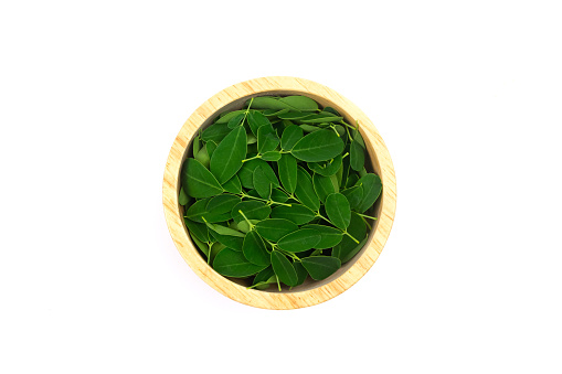 Moringa leaf on wooden bowl isolated on white background, top view. Moringa oleifera is both food and herbal medicine.