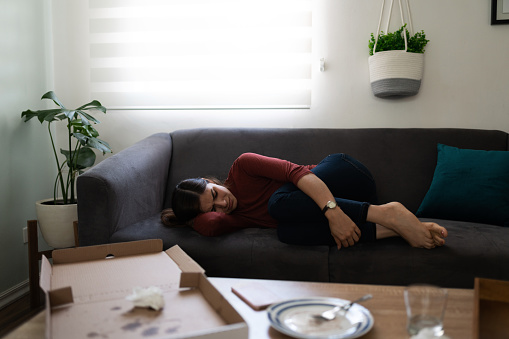 Depressed young woman lying on the couch with food an alcohol. Latin woman crying and having an emotional breakdown
