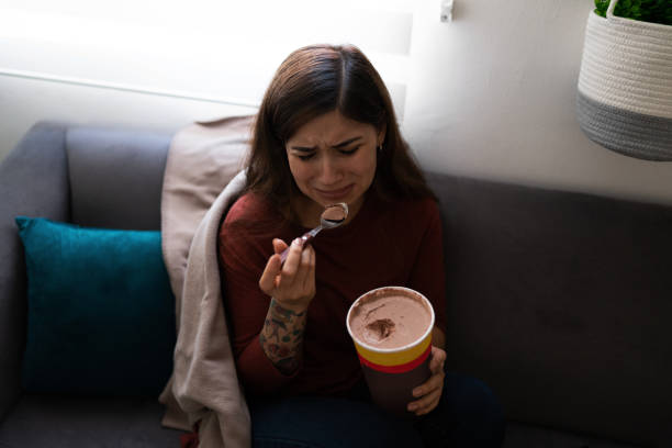 Lonely young woman crying and eating ice cream Depressed and heartbroken young latin woman eating chocolate ice cream while crying on the sofa. Hispanic woman feeling lonely brat stock pictures, royalty-free photos & images