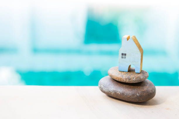 istock Blue wooden house model on stack of stone over blurred blue water background 1286439647