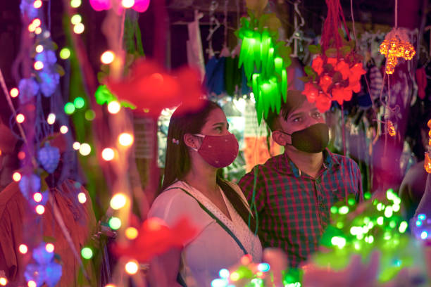 People buying decorative lighting for Diwali celebration inside a crowded marketplace in Kolkata Kolkata 11/13/2020: A young couple buying decorative lights, making last minute shopping for preparation of Kali puja and Diwali, wearing protective face masks. Varieties of multicoloured decorative lights & diyas are visible. Shot near Chandni Chowk, Esplanade, day before Kali puja. kolkata night stock pictures, royalty-free photos & images
