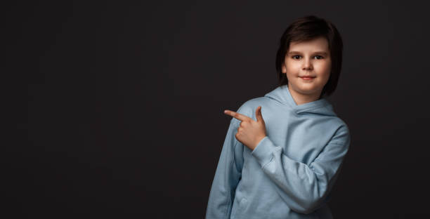 istock Cute boy shows his finger to the side, pointing copy space for your information. Studio shot, gray background 1286460990