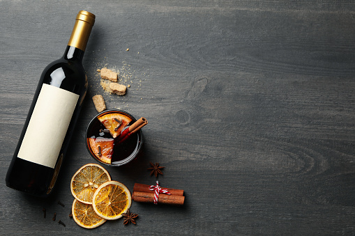 Bottle of wine, cup of mulled wine and ingredients on wooden background